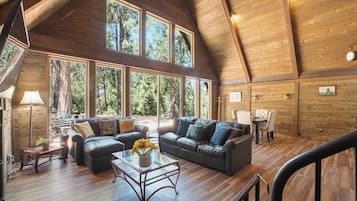 A spacious living area with a high ceiling and large windows, featuring a sofa set and a dining table.