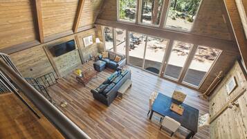 A spacious loft-style room with a large window, a sofa, a dining table, and a staircase.