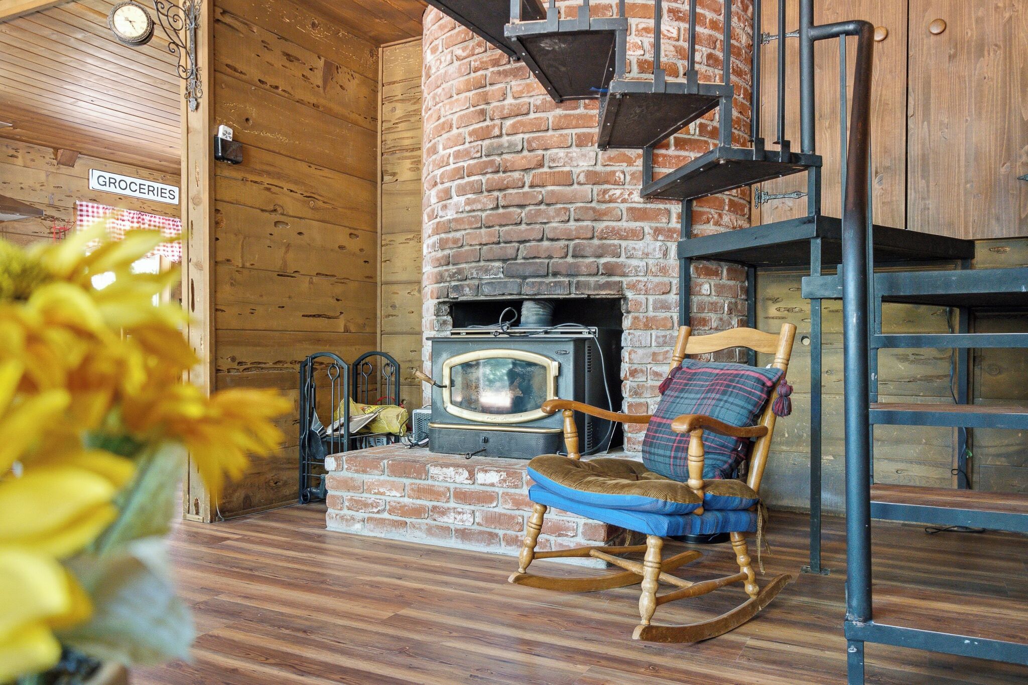 A rustic interior with a brick fireplace, a rocking chair, and a wooden floor.
