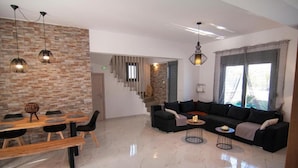 A modern living room with a dining area, a staircase, and a large window with curtains.