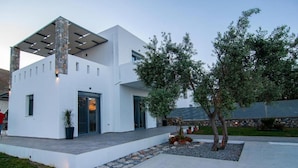 A modern white building with a stone facade, a covered patio, and a landscaped garden with trees and a stone pathway.