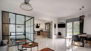 Un salon moderne avec une cloison en verre, une cuisine à l’arrière-plan et un coin repas offrant une vue dégagée.