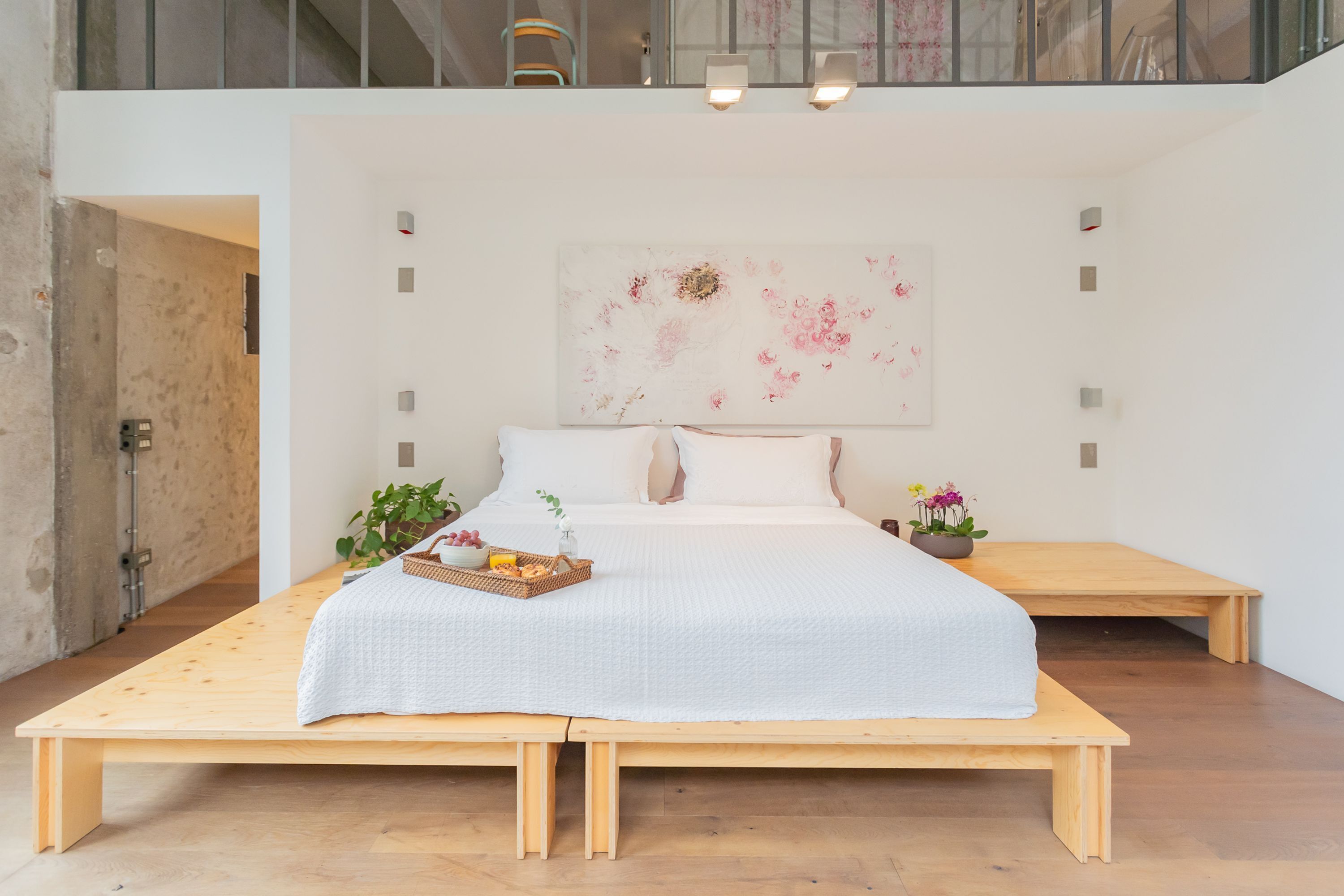A spacious bedroom with a large bed, wooden bench, and a wall-mounted light fixture.