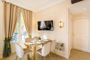 Een eetruimte met een tafel voor vier personen, een wandgemonteerde flatscreen televisie en een raam met gordijnen.
