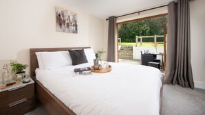 Un dormitorio con una cama grande, una mesita de noche, una ventana con cortinas y vistas al exterior.