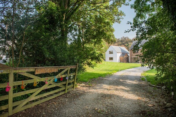 A gravel path leading to a white house with a stone exterior, surrounded by lush greenery and trees. - Robins Rest - Pets welcome - Free Parking - Back garden (Perranporth)