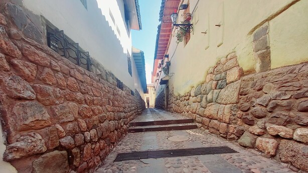 A narrow alleyway with stone walls and cobblestone pavement.