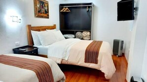A hotel room with two beds, a flat-screen TV mounted on the wall, a radiator, and a wooden floor.