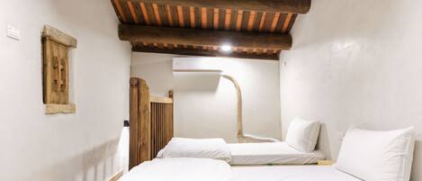 A room with two beds, a wooden ceiling, a small window, and an air conditioning unit.