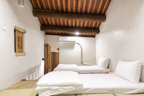 A room with two beds, a wooden ceiling, a small window, and an air conditioning unit.