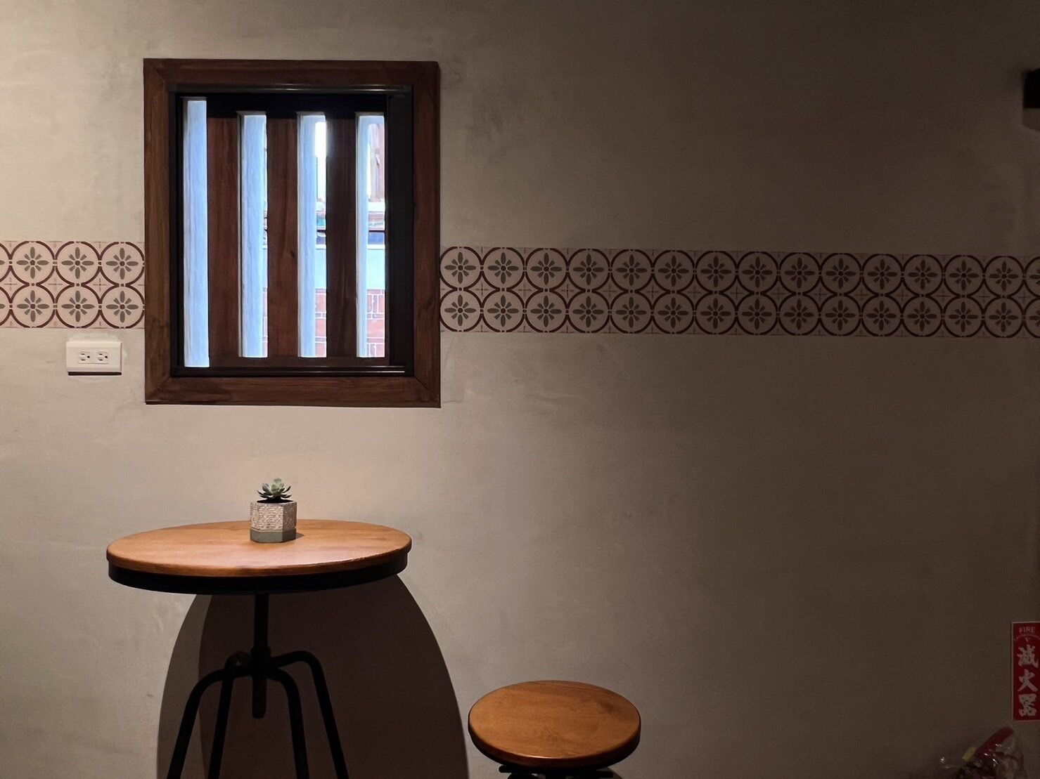 A small room with a window, a round table with a stool, and a patterned wall.