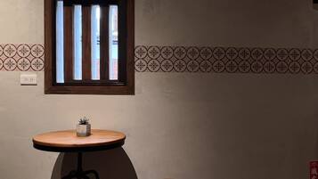 A small room with a window, a round table with a stool, and a patterned wall.