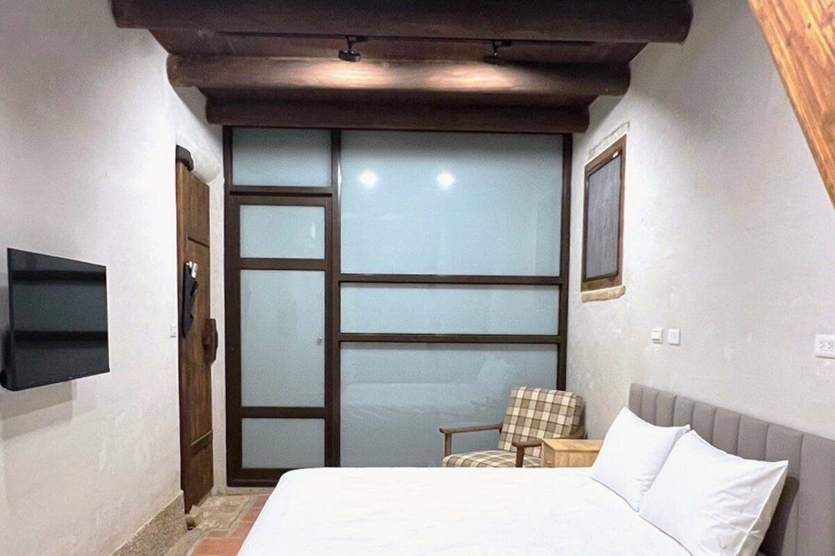 A bedroom with a bed, a chair, a nightstand, and a TV mounted on the wall.
