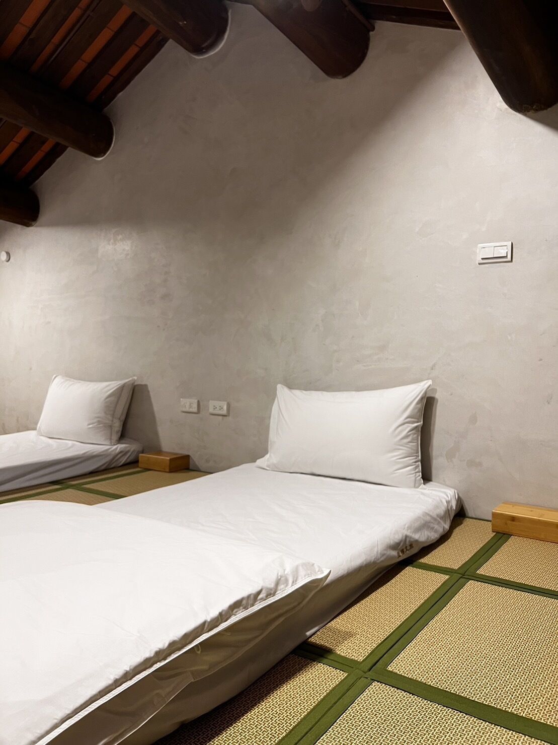 A room with two beds, a wooden ceiling, and a textured floor.
