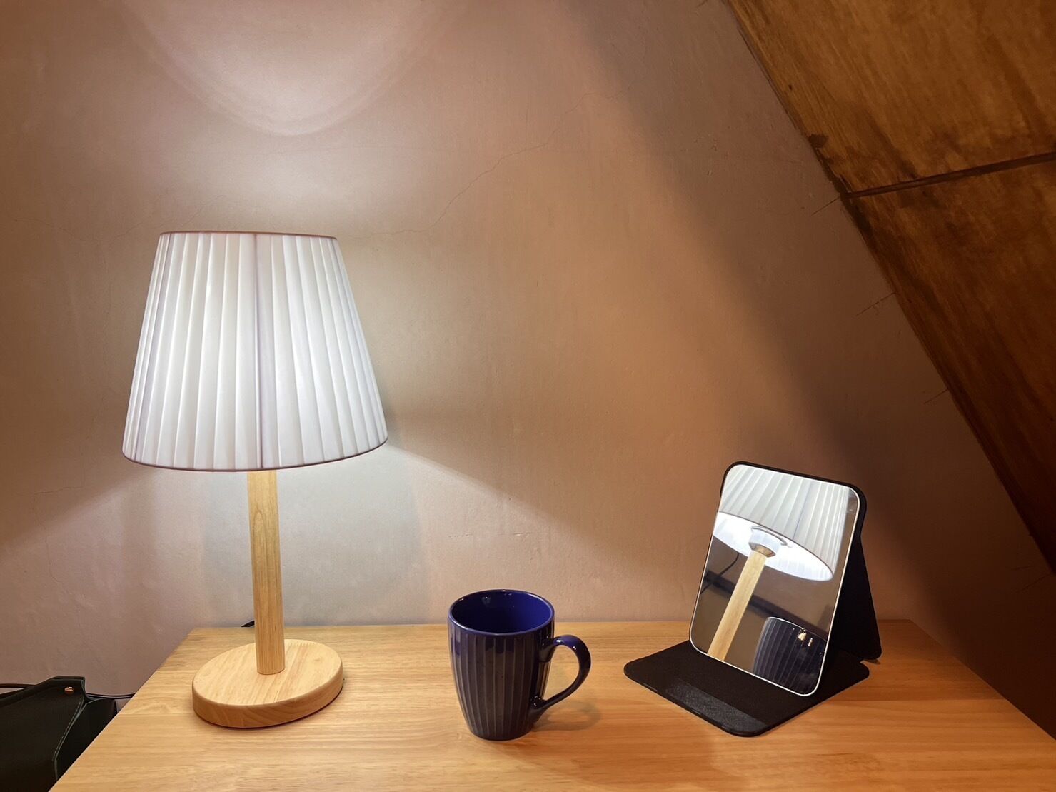 A wooden table with a lamp, a blue mug, and a mirror.
