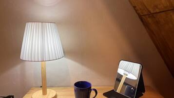 A wooden table with a lamp, a blue mug, and a mirror.