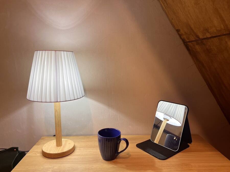 A wooden table with a lamp, a blue mug, and a mirror.