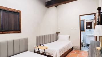 A small, cozy room with two beds, a small table, and a bathroom visible through an open door.