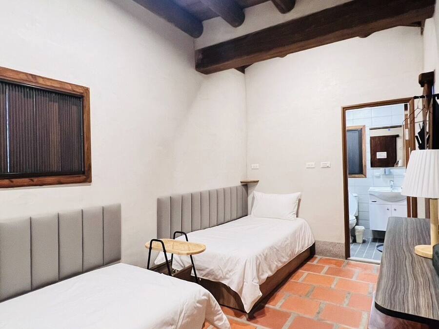 A small, cozy room with two beds, a small table, and a bathroom visible through an open door.