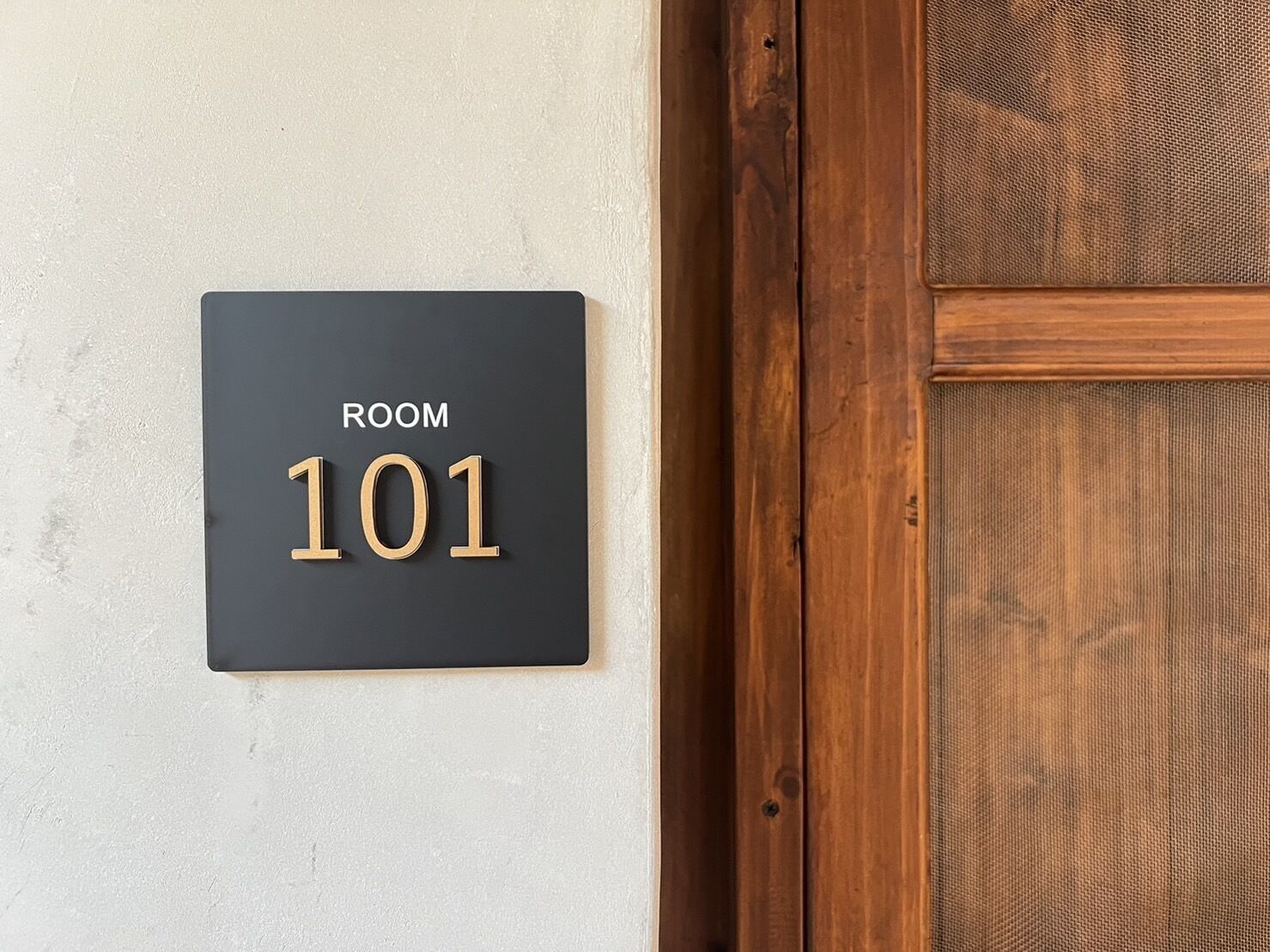 A black sign with "ROOM 101" on a light-colored wall, next to a wooden door with a textured panel.