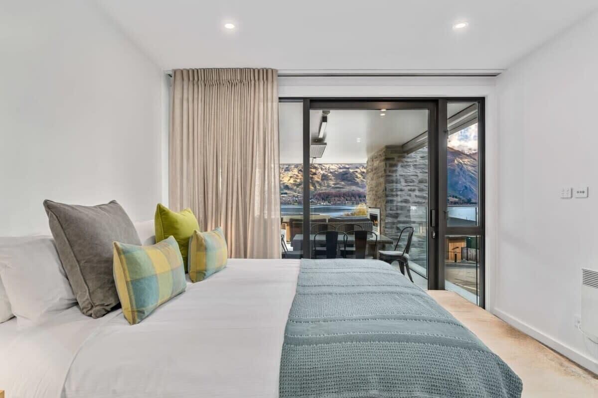 Une chambre à coucher avec un lit, des oreillers, une fenêtre avec des rideaux et une vue sur un paysage montagneux.