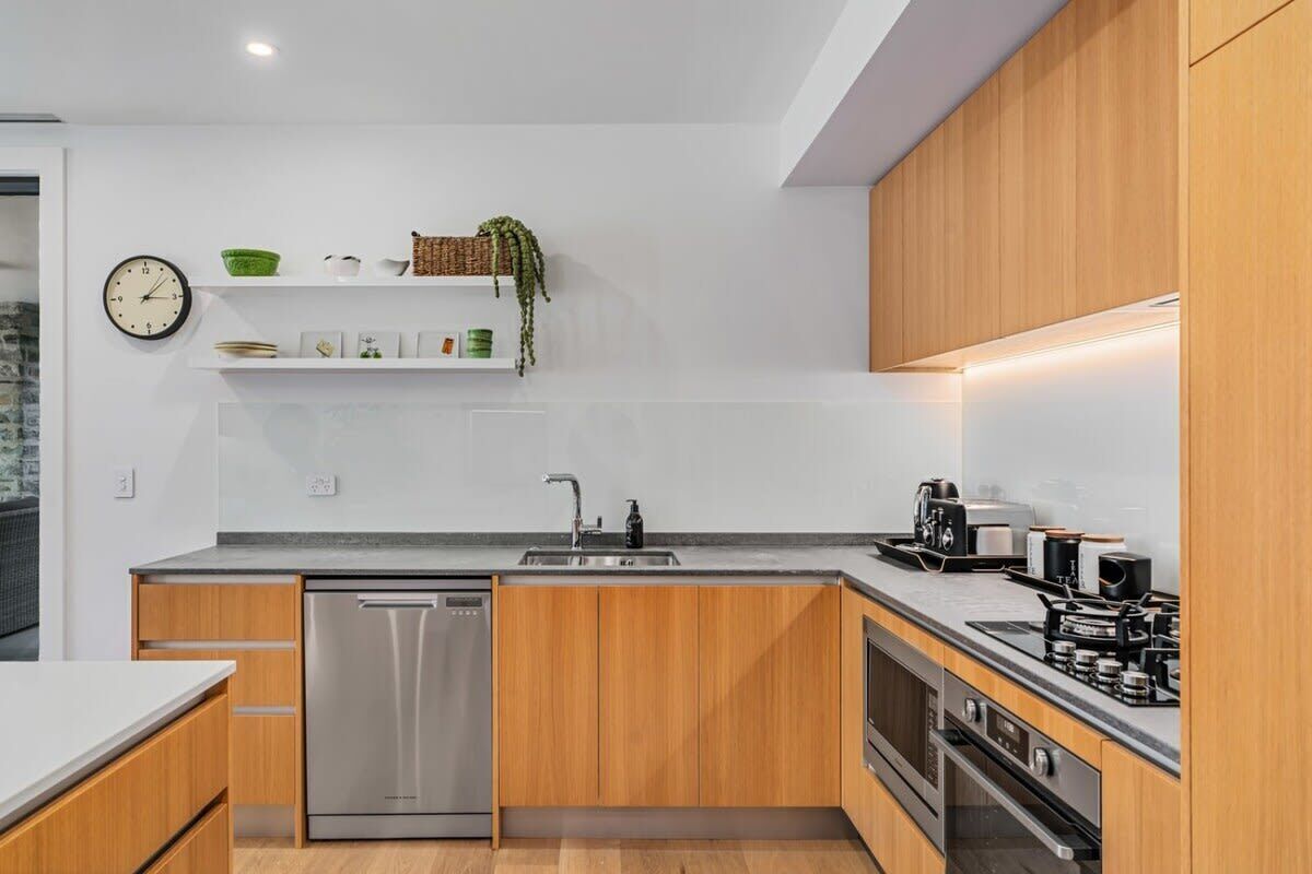 A modern kitchen with wooden cabinets, a stainless steel dishwasher, a sink, and a stove.