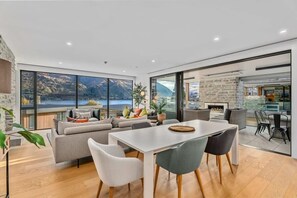 Un salon moderne dotĂ© dâune grande fenĂȘtre, dâun coin repas et dâune cuisine visible Ă travers des portes vitrĂ©es.