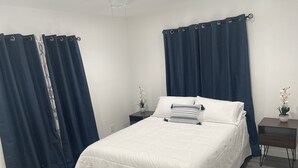 A neatly made bed with white bedding, two bedside tables with potted plants, and dark blue curtains. - 3-bedroom farm stay just 13 minutes from Santa Anita Park (Azusa)