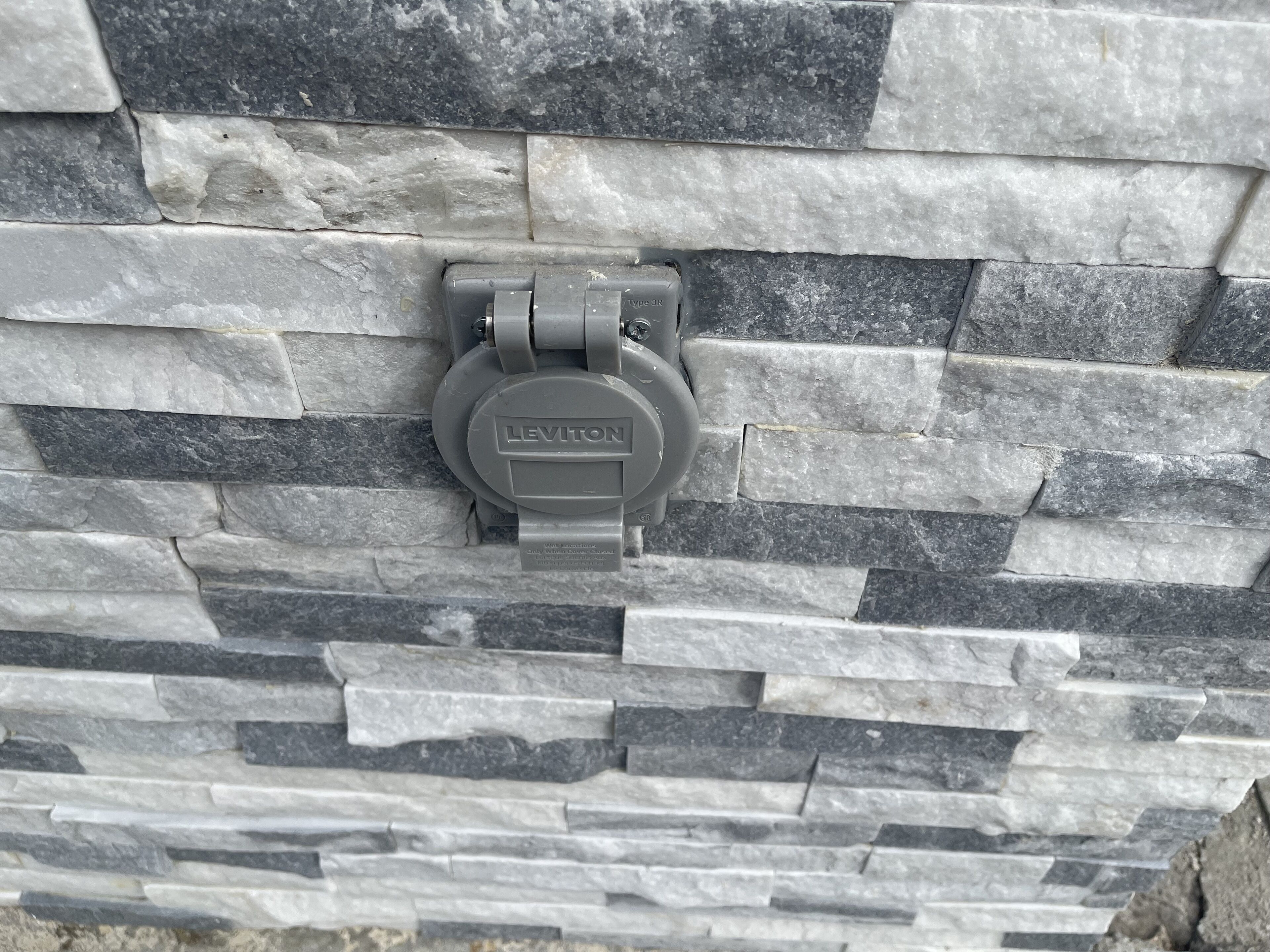 A stone wall with a Leviton electrical box.