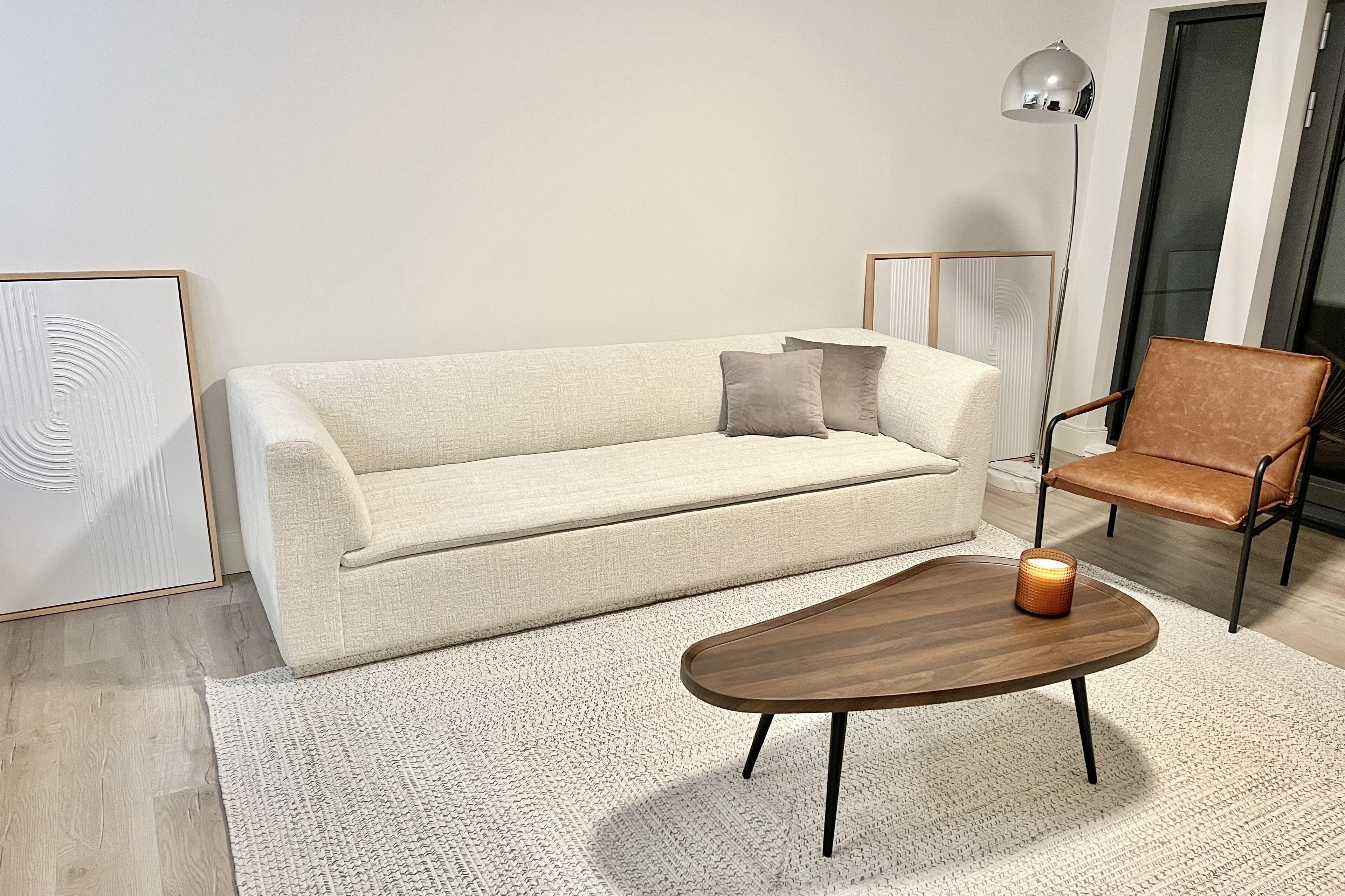 A modern living room with a beige sofa, a wooden coffee table, a brown leather chair, and a floor lamp.