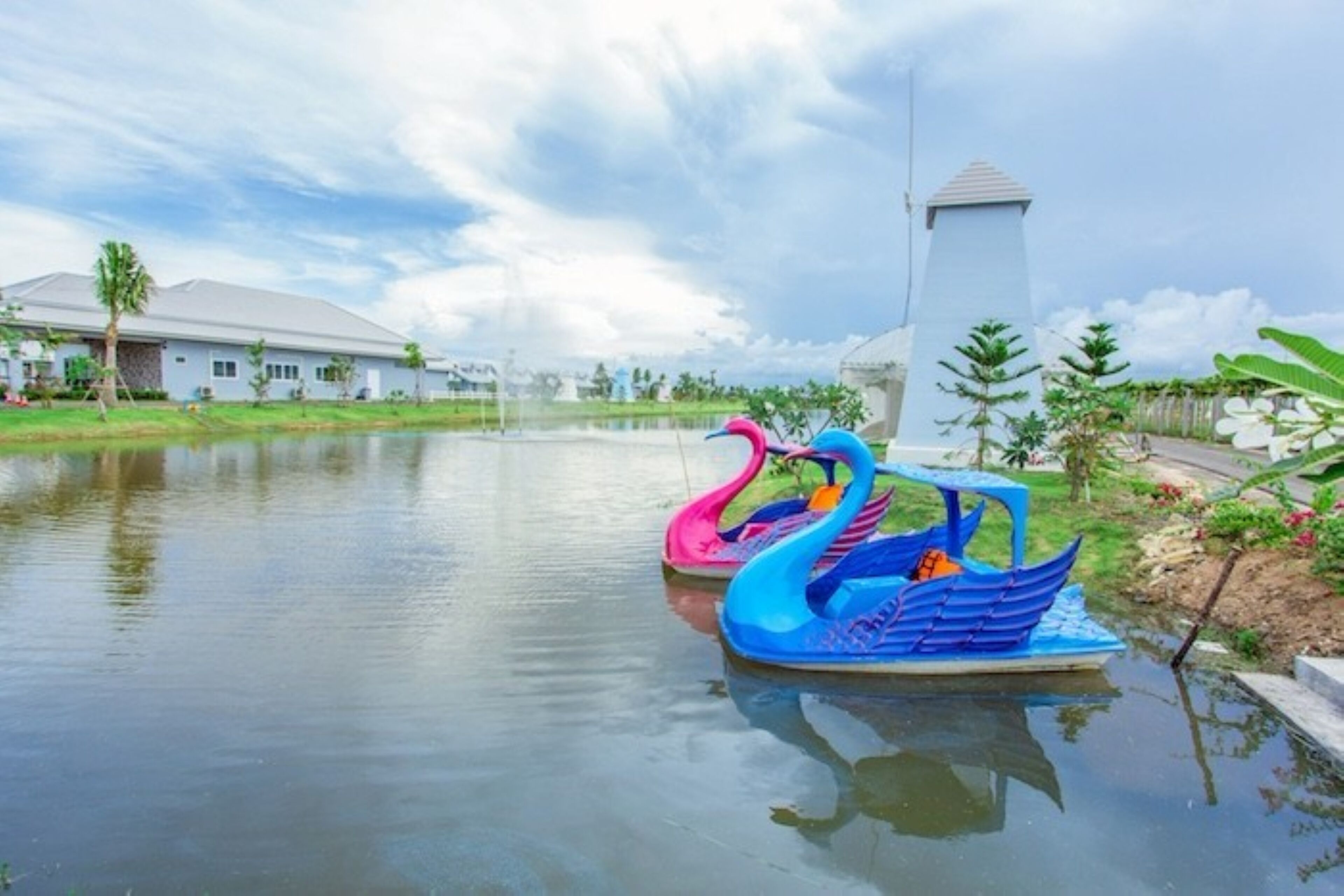 A calm water body with two colorful swan-shaped boats, a white building, and a tower in the background.