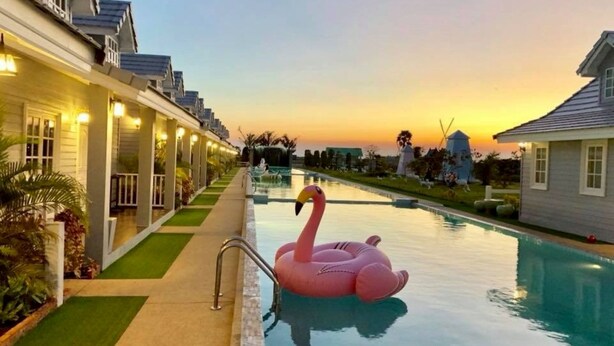 Une piscine avec un flotteur en forme de flamant rose, entourée de bâtiments d’hôtel et avec un coucher de soleil en arrière-plan.