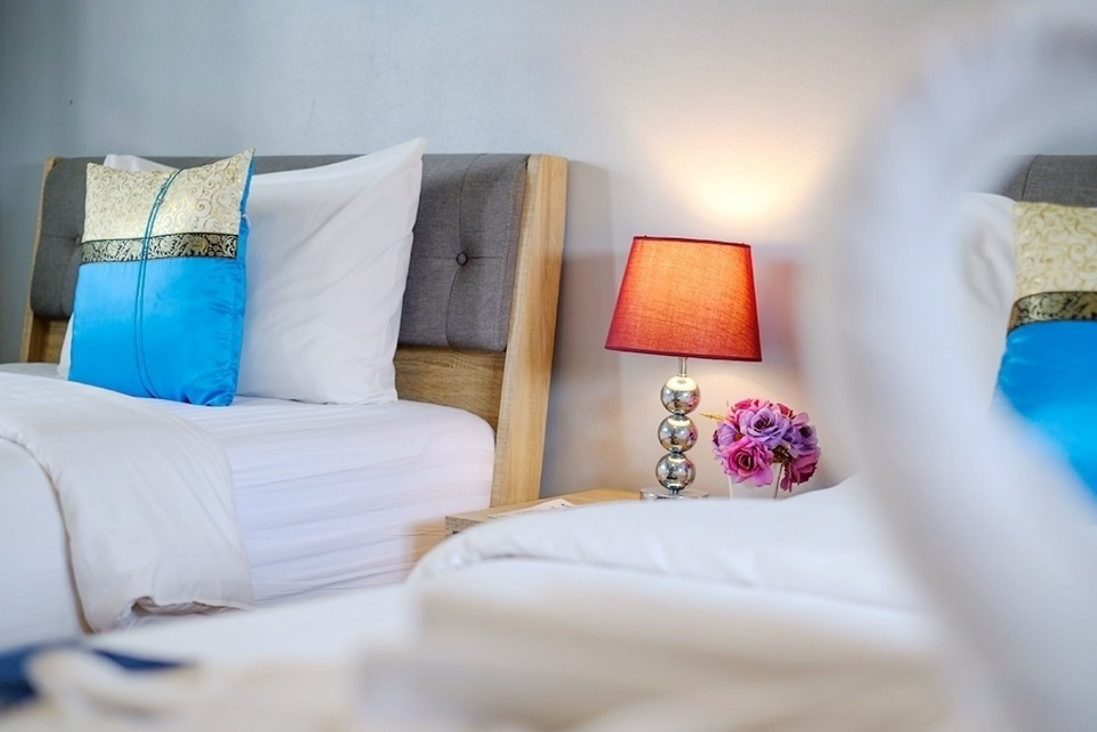 A hotel room with two beds, a nightstand with a lamp, and a vase with flowers.