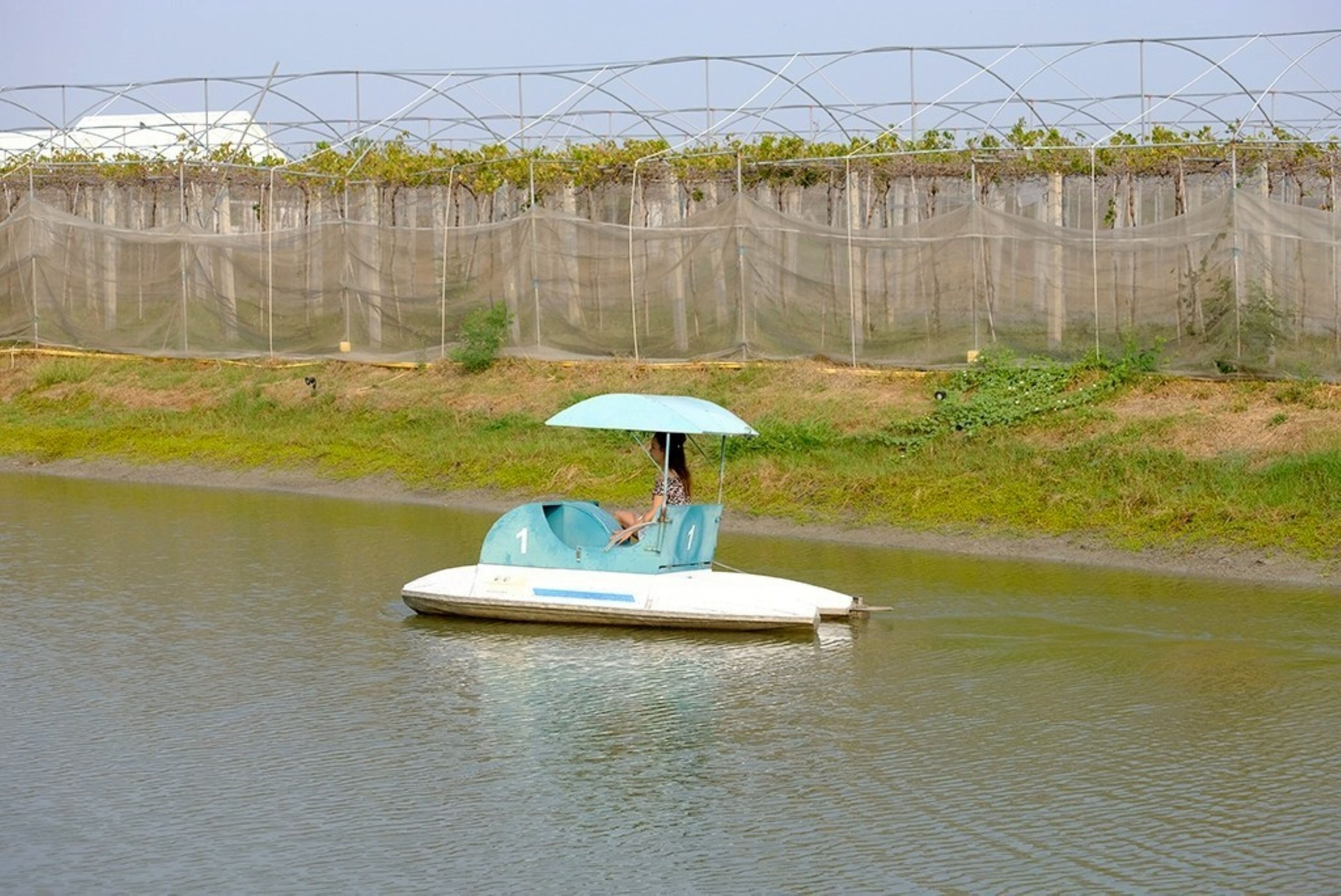 Un bote con una persona sosteniendo un paraguas en un río tranquilo.