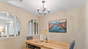 Un comedor con mesa y bancos de madera, una araña, un cuadro de un paisaje urbano y un ventanal con vista a un edificio.