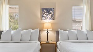 Una habitación de hotel con dos camas individuales, una mesita de noche con lámpara y una obra de arte floral en la pared.