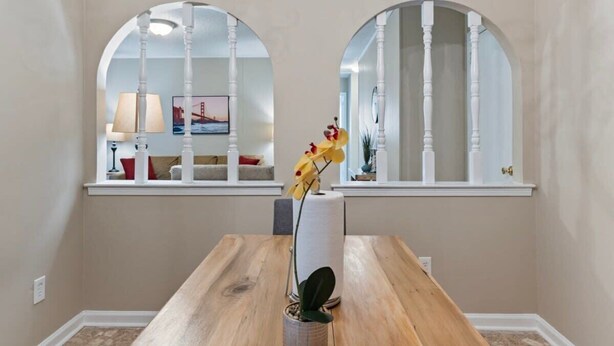 Comedor con mesa de madera y dos ventanas arqueadas con marcos blancos.