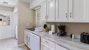 Una cocina con armarios blancos, lavavajillas, cafetera y tostadora.