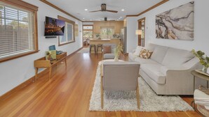 A spacious living room with a sofa, a coffee table, and a TV. There is a kitchen in the background with wooden cabinets and a dining area. - Canyonview Craftsman Near All Things San Diego! (San Diego)