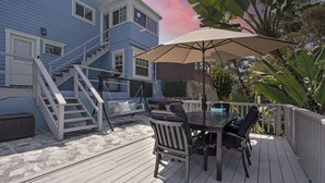 Um terraço com mesa e cadeiras, um guarda-sol e uma escadaria que leva a uma casa azul.