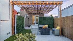 Ein überdachter Patio-Bereich mit einem Feuertisch, Gartenmöbeln und einem Holzzaun.