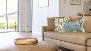 A living room with a beige sofa, two patterned throw pillows, a wooden tray, and a red patterned rug. - Bimbajong Studio - Pet Friendly- Oceanstays (Yamba)