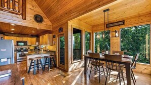 A wooden cabin interior with a kitchen, dining area, and large windows. - Private Mtn Views|Movie Theater|Hot Tub|Pool Table (Sevierville)