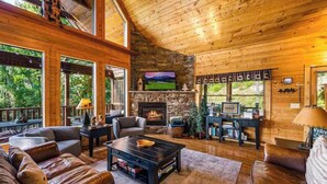 A spacious living room with a stone fireplace, leather sofas, and a large window overlooking greenery. - Private Mtn Views|Movie Theater|Hot Tub|Pool Table (Sevierville)