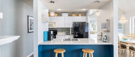 A modern kitchen with white cabinets, a blue accent wall, a black refrigerator, and two wooden stools.