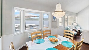 Spiseområde med udsigt over vandet, en lysekrone og et bord dækket med blå servietringe og en skål med pasta.