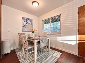 Un comedor con una mesa dispuesta para cuatro, un cuadro en la pared y una ventana con persianas.