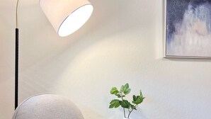 Un fauteuil moderne doté d’un dossier tissé, placé à côté d’un lampadaire et d’une petite table sur laquelle se trouve une plante.