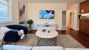 Un salon moderne avec un grand téléviseur à écran plat fixé au mur, un canapé bleu, une table basse ronde et une plante en pot.