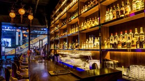A bar area with shelves of liquor bottles, bar stools, and a counter. - fuan hotel (Shenzhen)